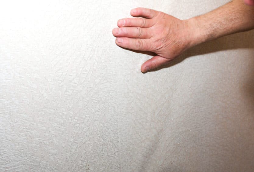 Main inspectant un mur intérieur pour détecter l’humidité dans une maison